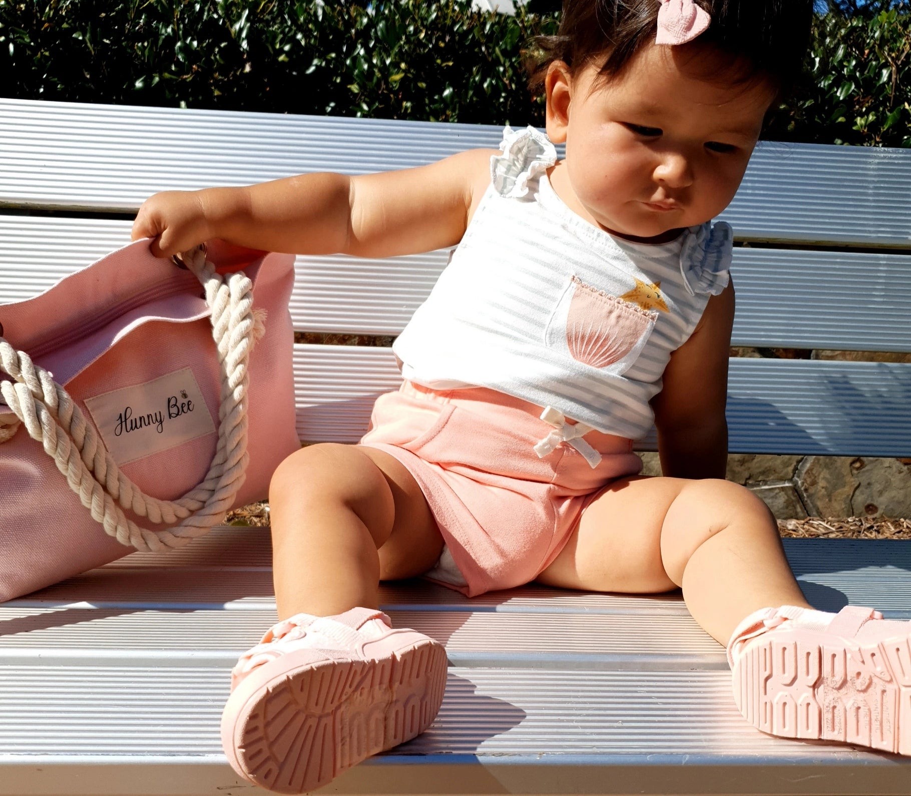 Toddler holding Child pink tote bag and shitting on park bench 