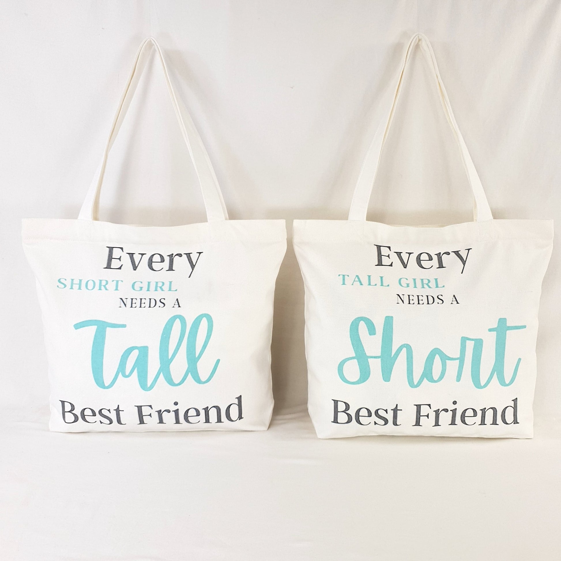Tall Friend and Short Friend bags, one bag print text reads : "Every Short girl needs a tall best friend" and the words "short girl" and "Tall" is in Teal color and rest of writing is in dark grey. the other bag print reads: "Every tall girl needs a short best friend" colouring of the print text is the same as the other bag.  Bag itself is white with shoulder straps, zipper on the top